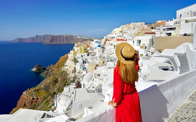 Woman in red dress overlooking white buildings and sea in Oia, Santorini.
