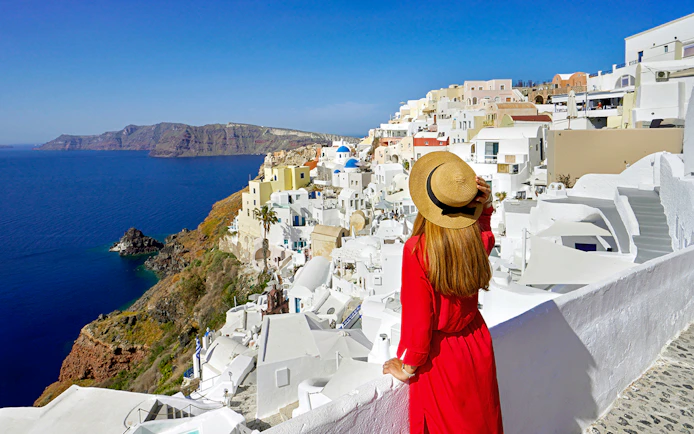 Woman in red dress overlooking white buildings and sea in Oia, Santorini.