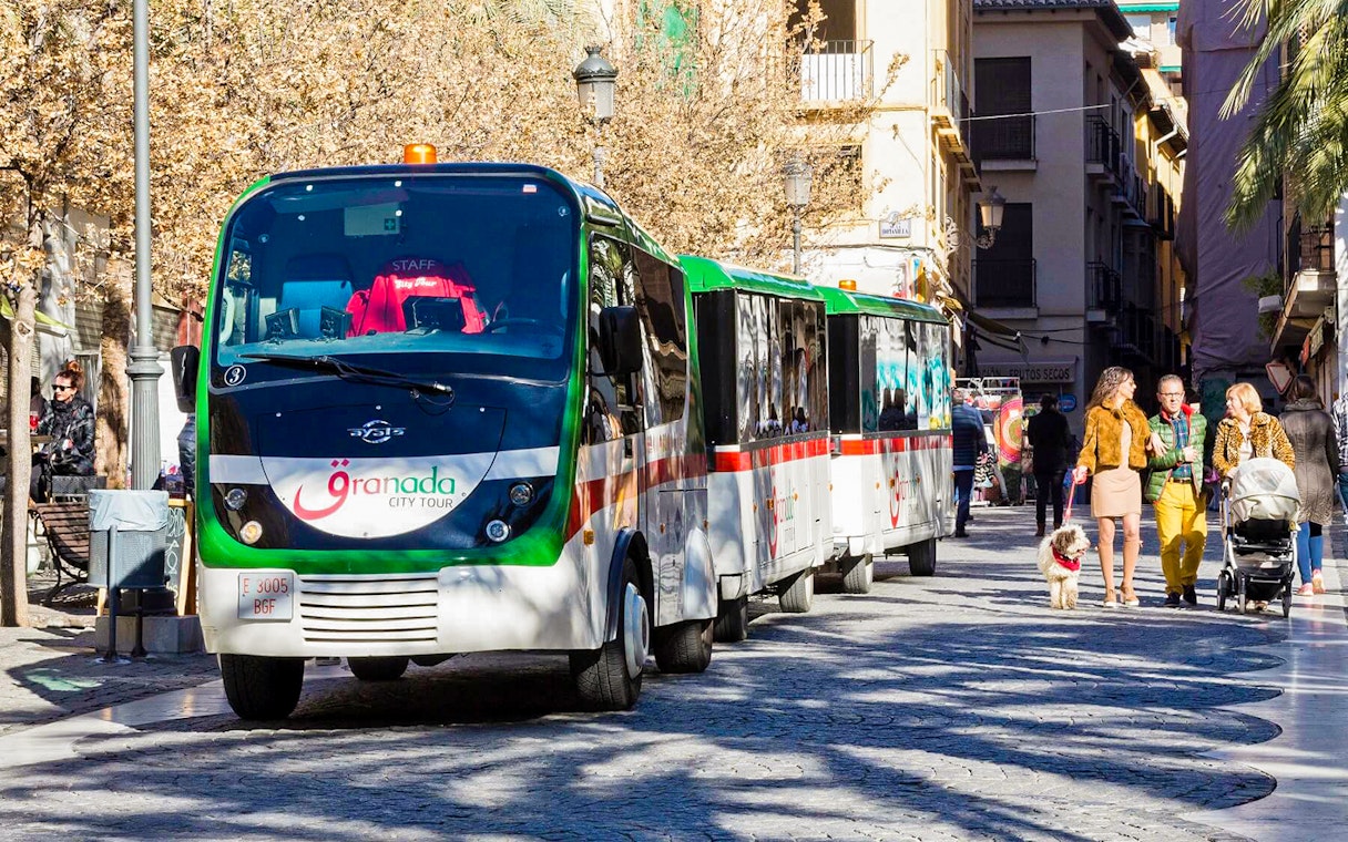 Granada city tour bus on a cobblestone street with people walking nearby.