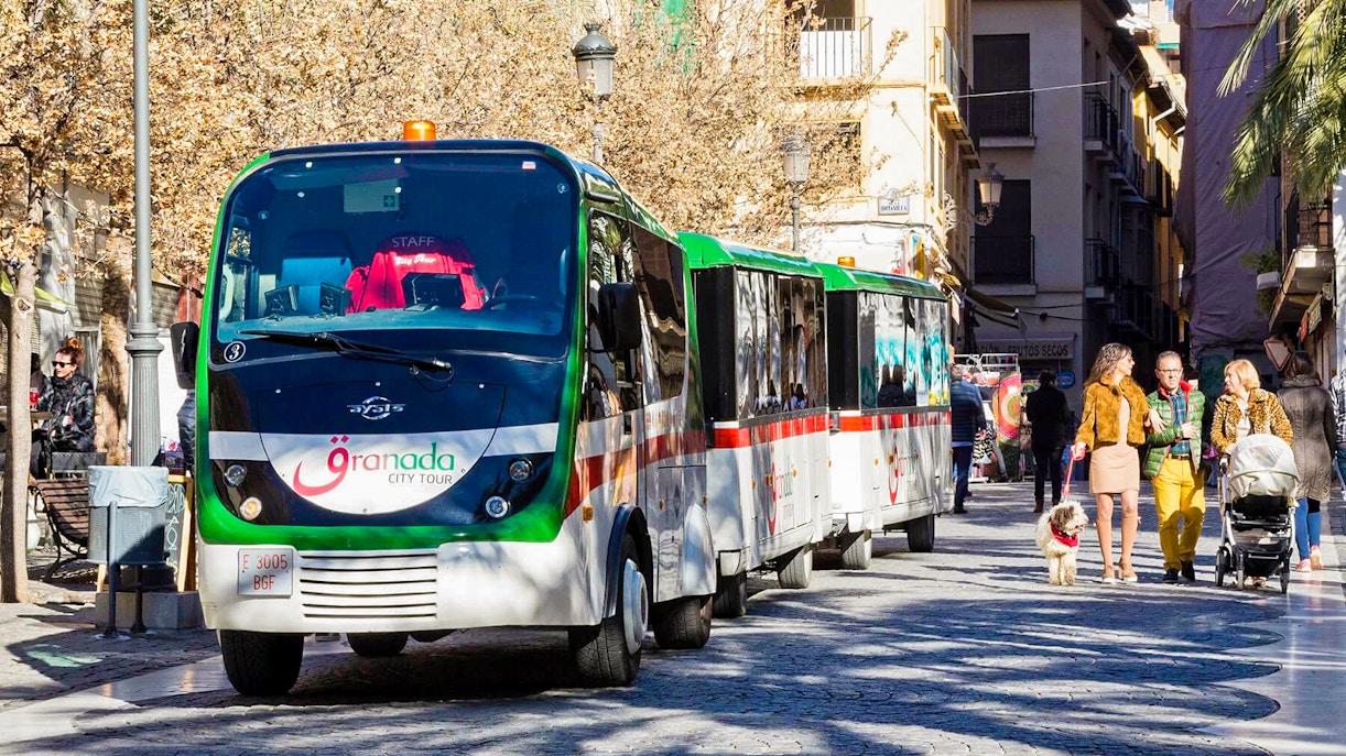 Granada city tour bus on a cobblestone street with people walking nearby.