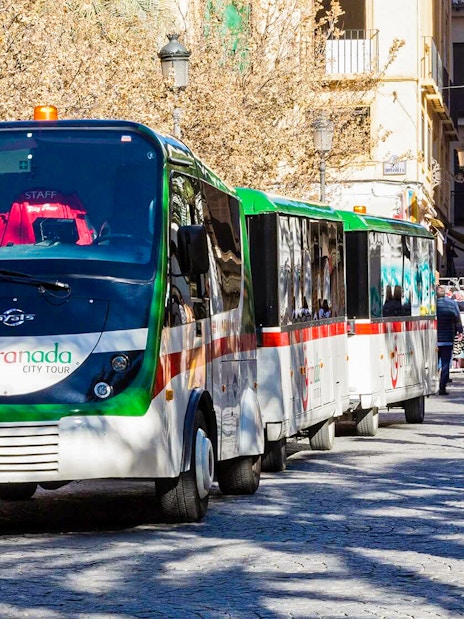 Granada city tour bus on a cobblestone street with people walking nearby.