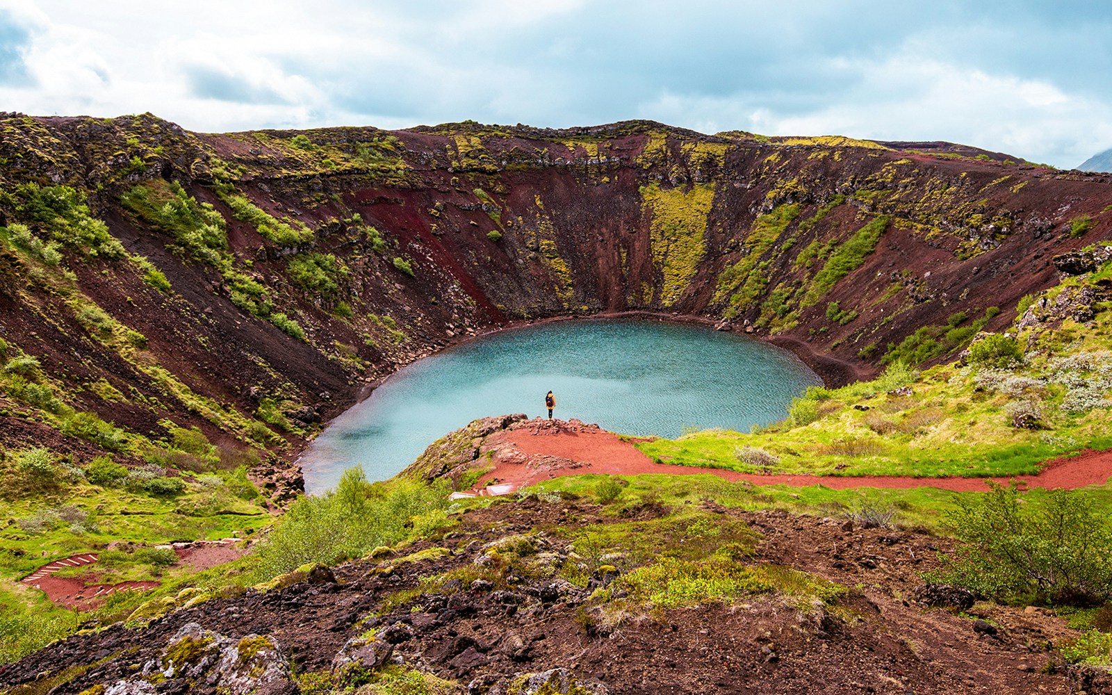 Kerid Crater Lake in Iceland with vibrant blue water surrounded by red volcanic rock.