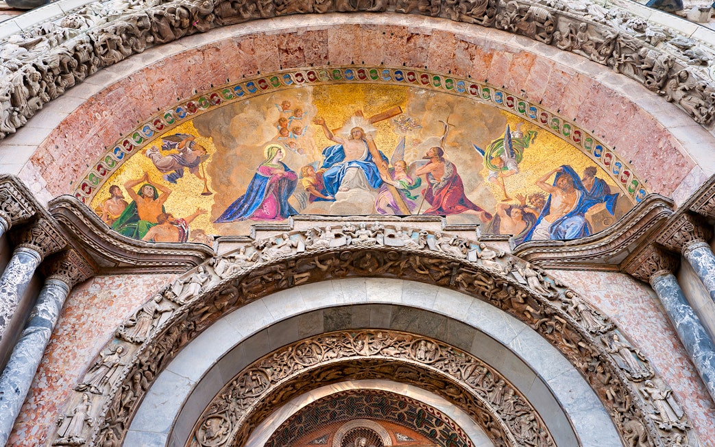 Mosaic detail above entrance of St Mark's Basilica, Venice, featuring religious figures and intricate carvings.