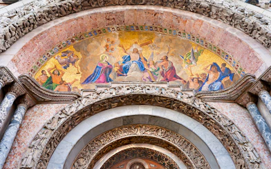 Mosaic detail above entrance of St Mark's Basilica, Venice, featuring religious figures and intricate carvings.