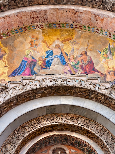 Mosaic detail above entrance of St Mark's Basilica, Venice, featuring religious figures and intricate carvings.