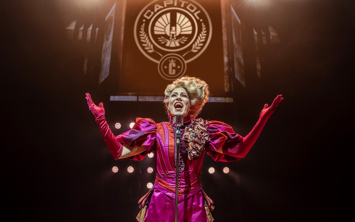 Performer in vibrant costume on stage during Hunger Games West End show.
