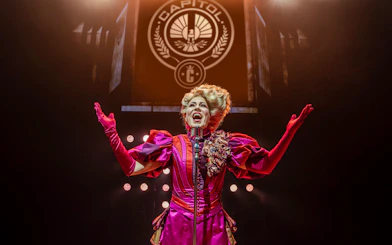 Performer in vibrant costume on stage during Hunger Games West End show.