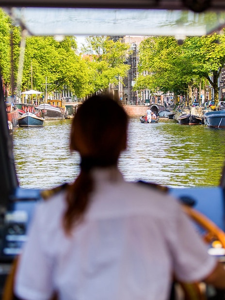 Boat captain navigating Amsterdam canal on City Sightseeing Hop-On Hop-Off tour.