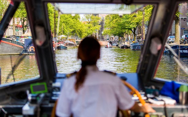Boat captain navigating Amsterdam canal on City Sightseeing Hop-On Hop-Off tour.