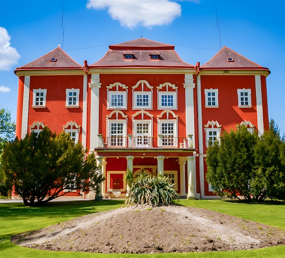 Red building with white trim surrounded by green lawn and trees under a blue sky.