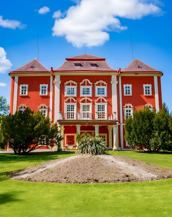 Red building with white trim surrounded by green lawn and trees under a blue sky.