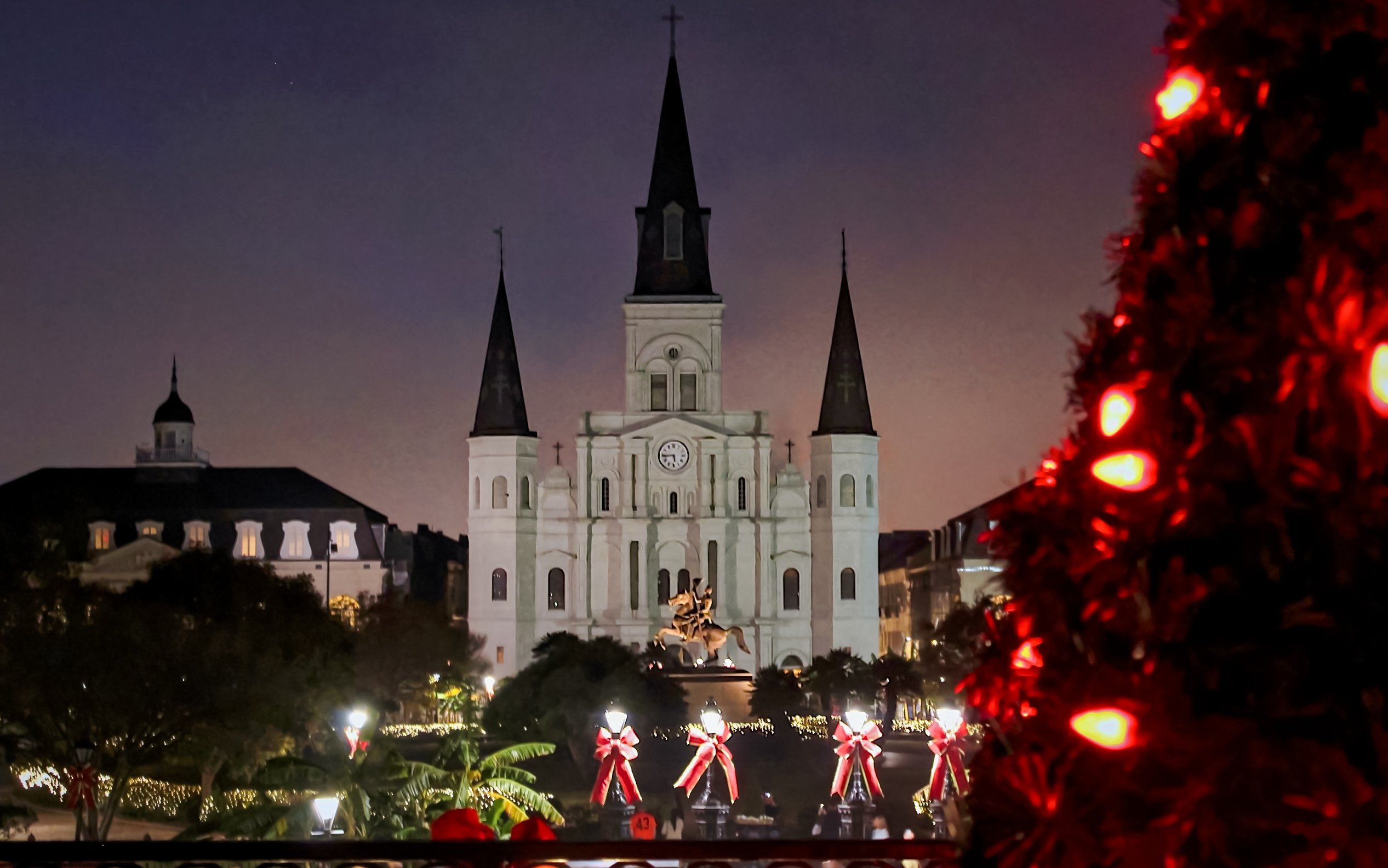 Jackson Square in New Orleans decorated with Christmas lights and a lit tree in the foreground.