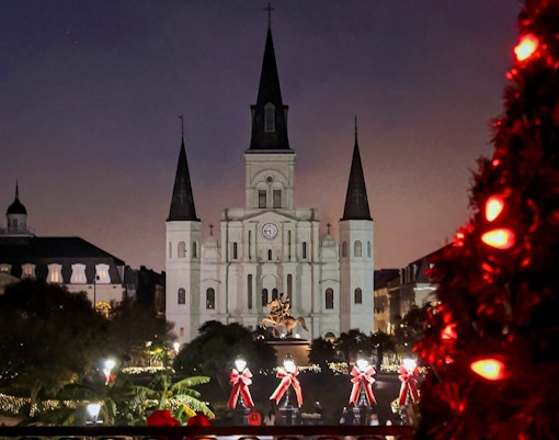 Jackson Square in New Orleans decorated with Christmas lights and a lit tree in the foreground.