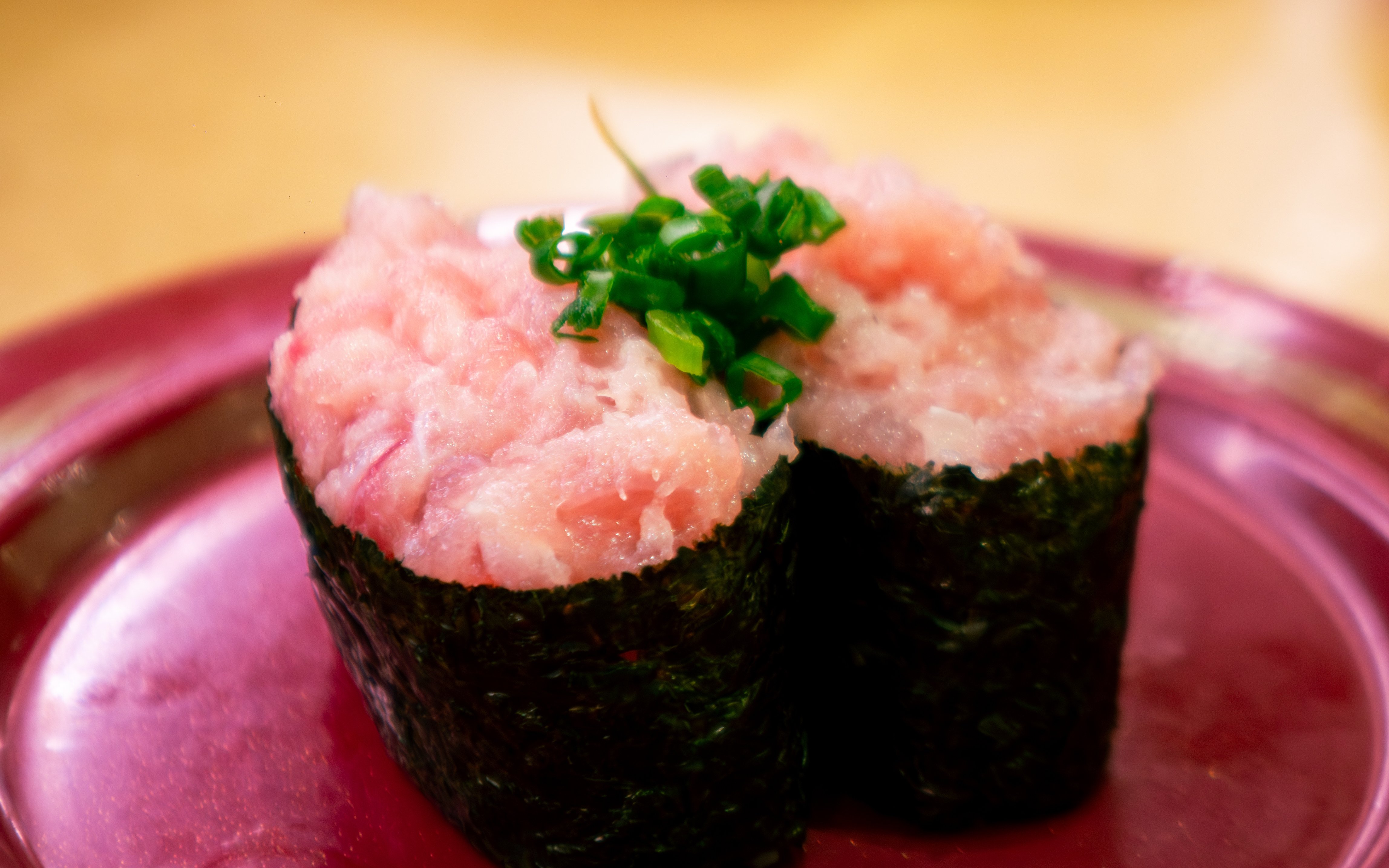 Negitoro gunkan maki sushi with minced fatty tuna and green onion on red plate.