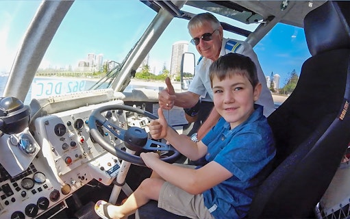 Child and guide giving thumbs up inside Aquaduck vehicle, Sunshine Coast skyline visible.