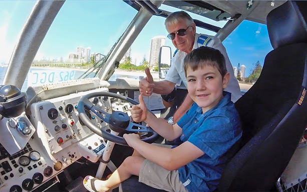 Child and guide giving thumbs up inside Aquaduck vehicle, Sunshine Coast skyline visible.