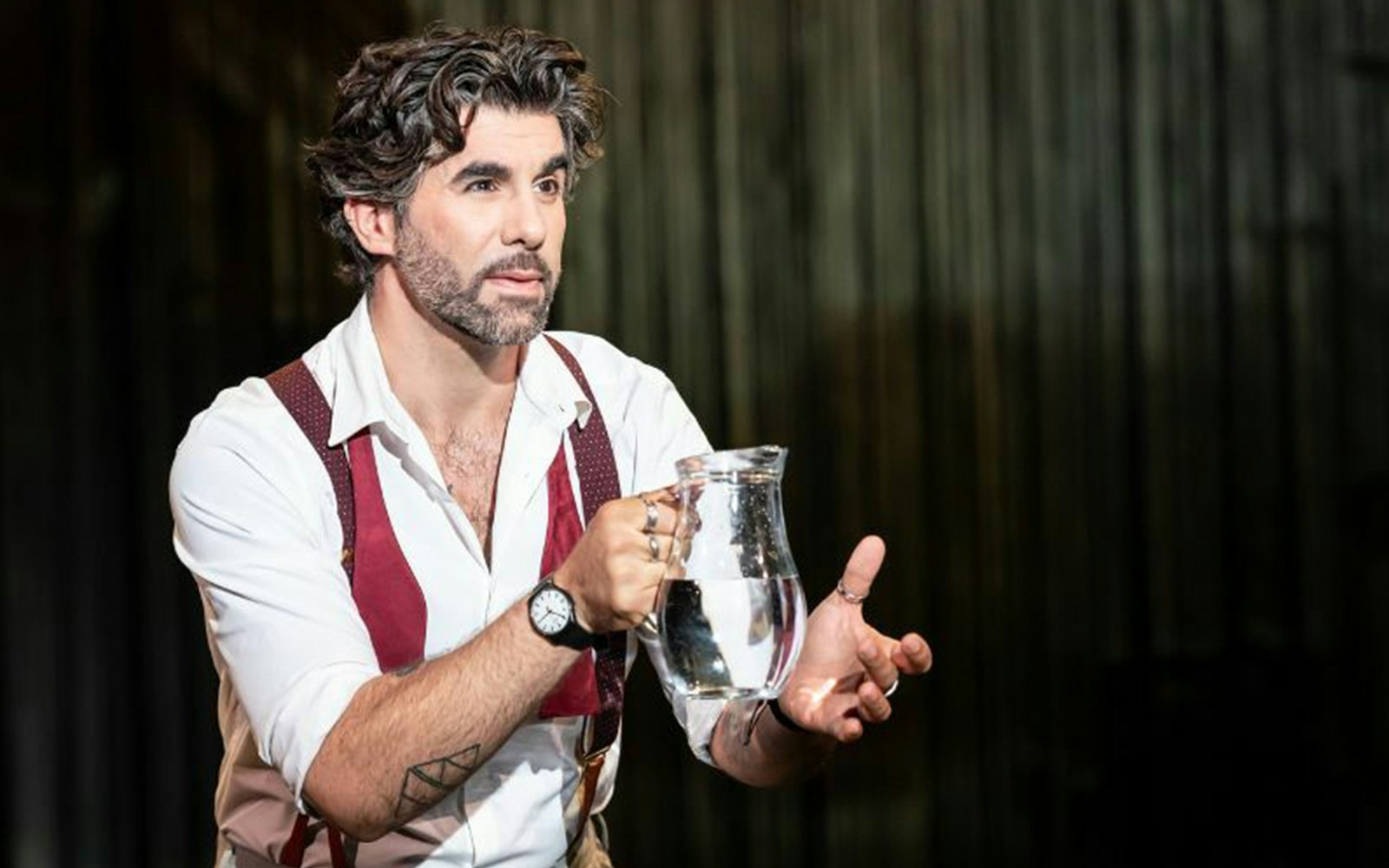 Man holding a glass pitcher during a theatrical performance.