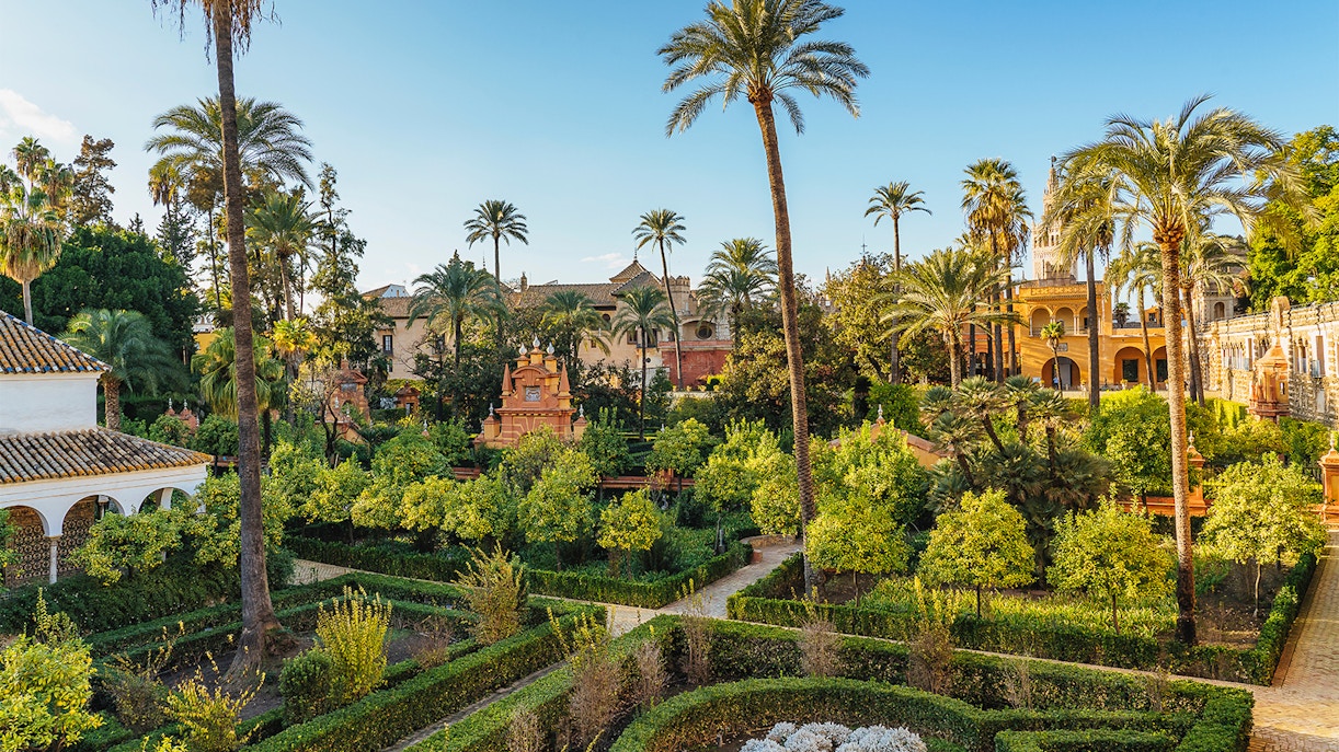 Tourists exploring the stunning architecture of Alcazar of Seville, with a view of Seville Cathedral and Giralda in the background, available with skip-the-line tickets