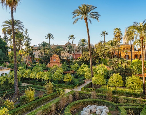 Tourists exploring the stunning architecture of Alcazar of Seville, with a view of Seville Cathedral and Giralda in the background, available with skip-the-line tickets
