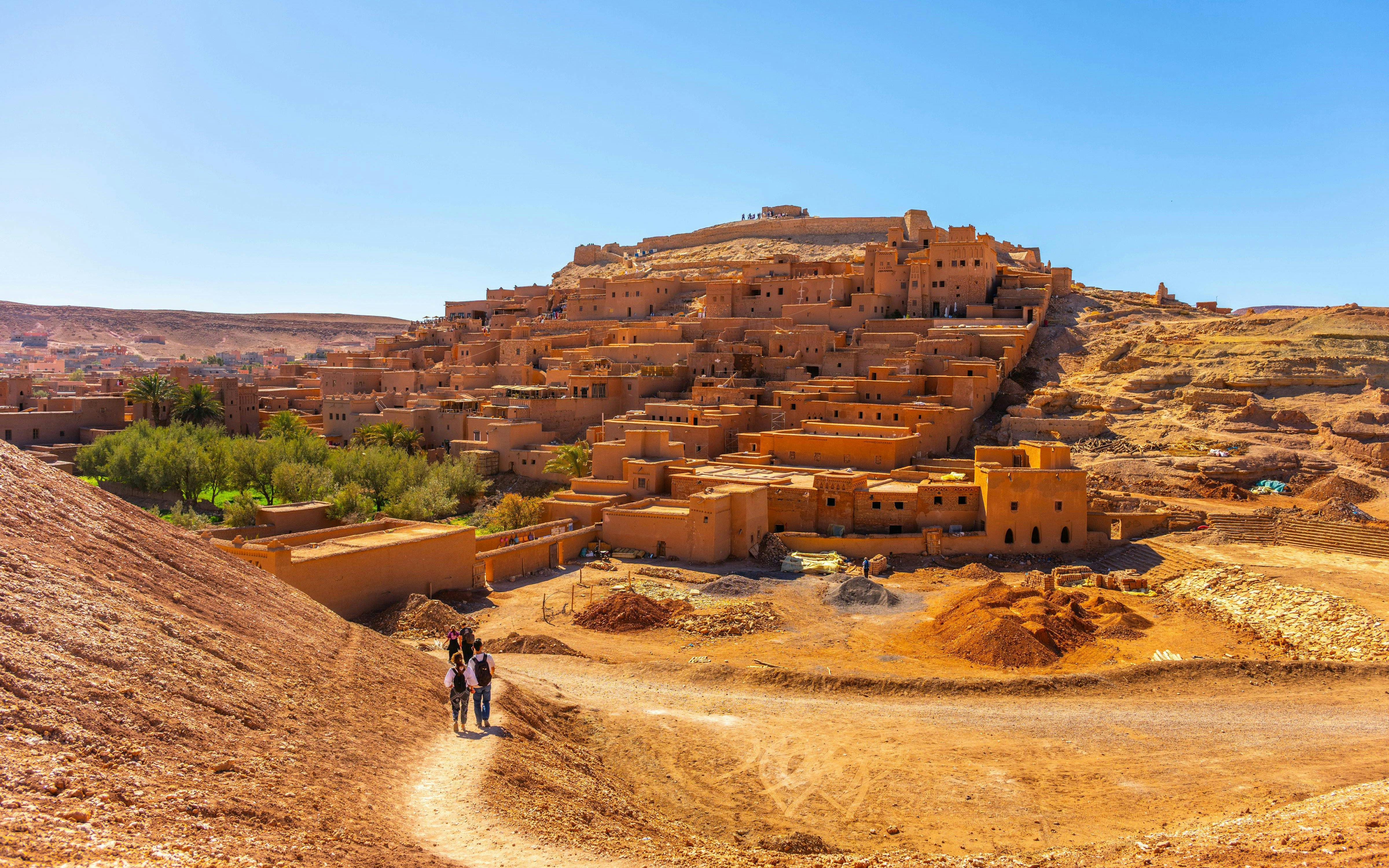 Visitors walking on a path towards the ancient kasbah of Ait Benhaddou, Morocco.