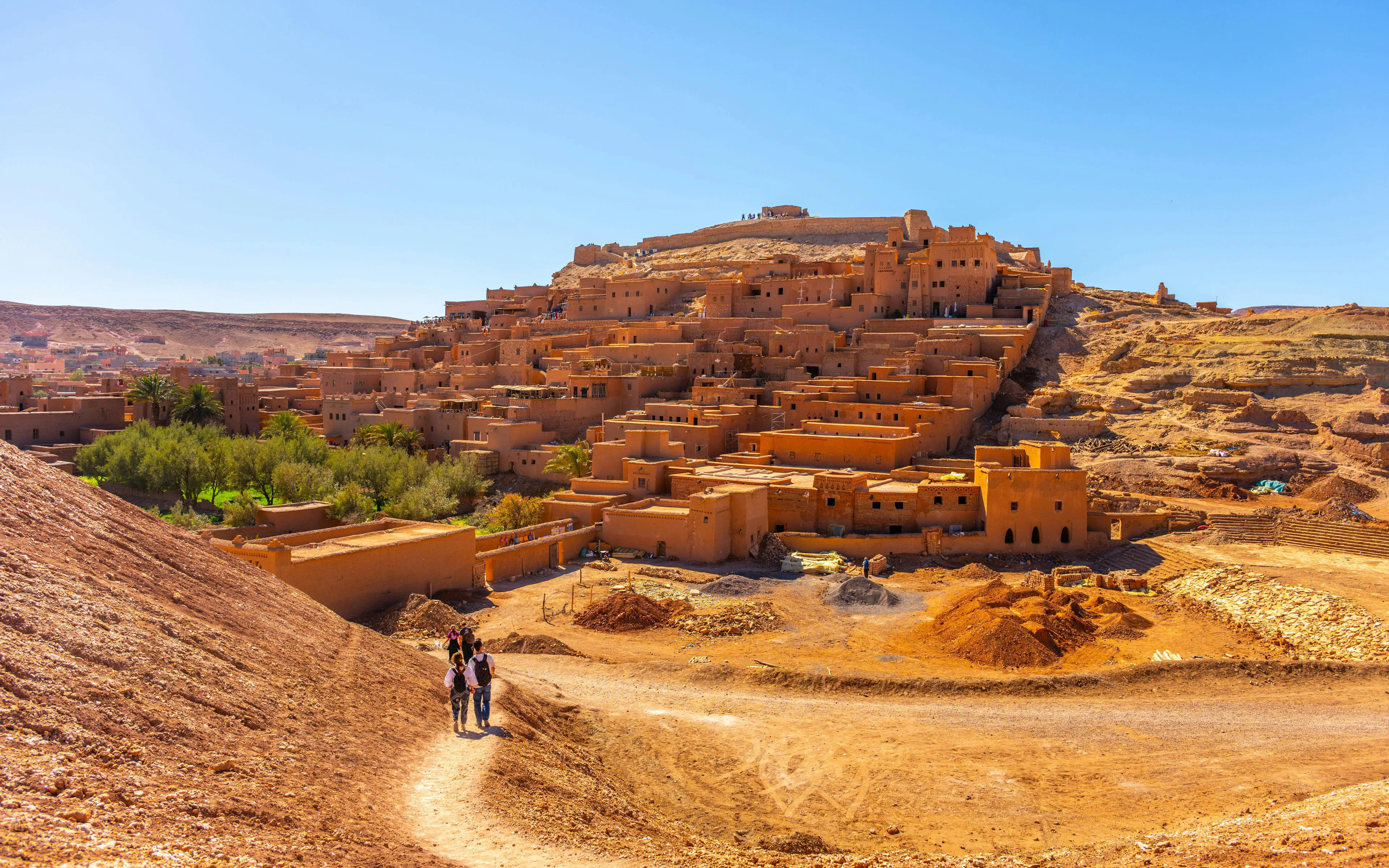 Visitors walking on a path towards the ancient kasbah of Ait Benhaddou, Morocco.