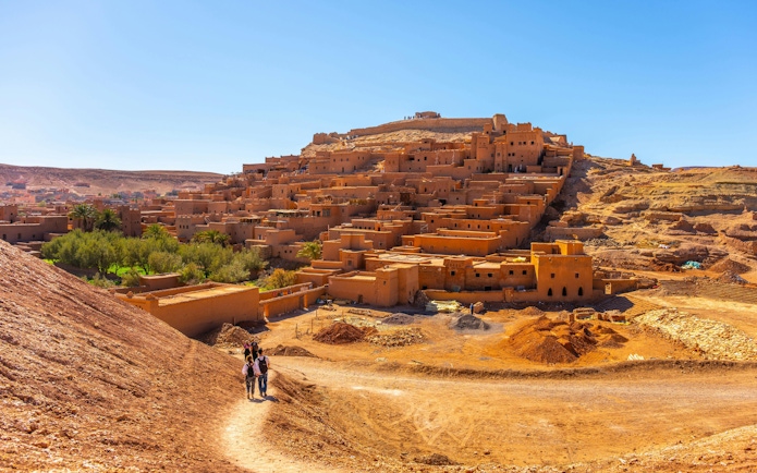 Visitors walking on a path towards the ancient kasbah of Ait Benhaddou, Morocco.