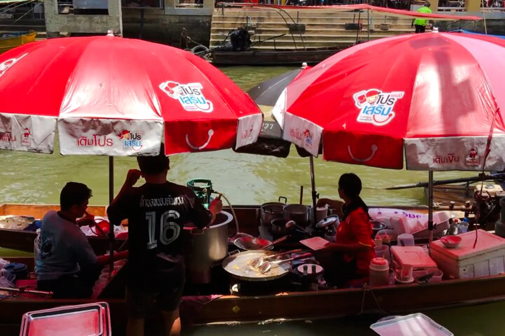 Vendors cooking under red umbrellas at Amphawa Floating Market, Thailand.