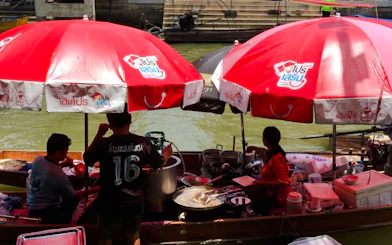 Vendors cooking under red umbrellas at Amphawa Floating Market, Thailand.