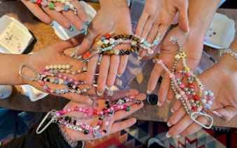 Hands displaying colorful handmade bracelets and necklaces at a workshop in Essaouira.