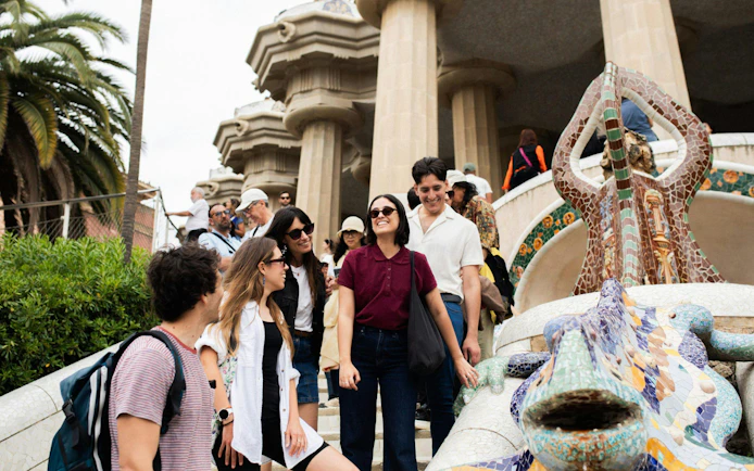 Tourists with guide at Park Güell near mosaic lizard sculpture, Barcelona.