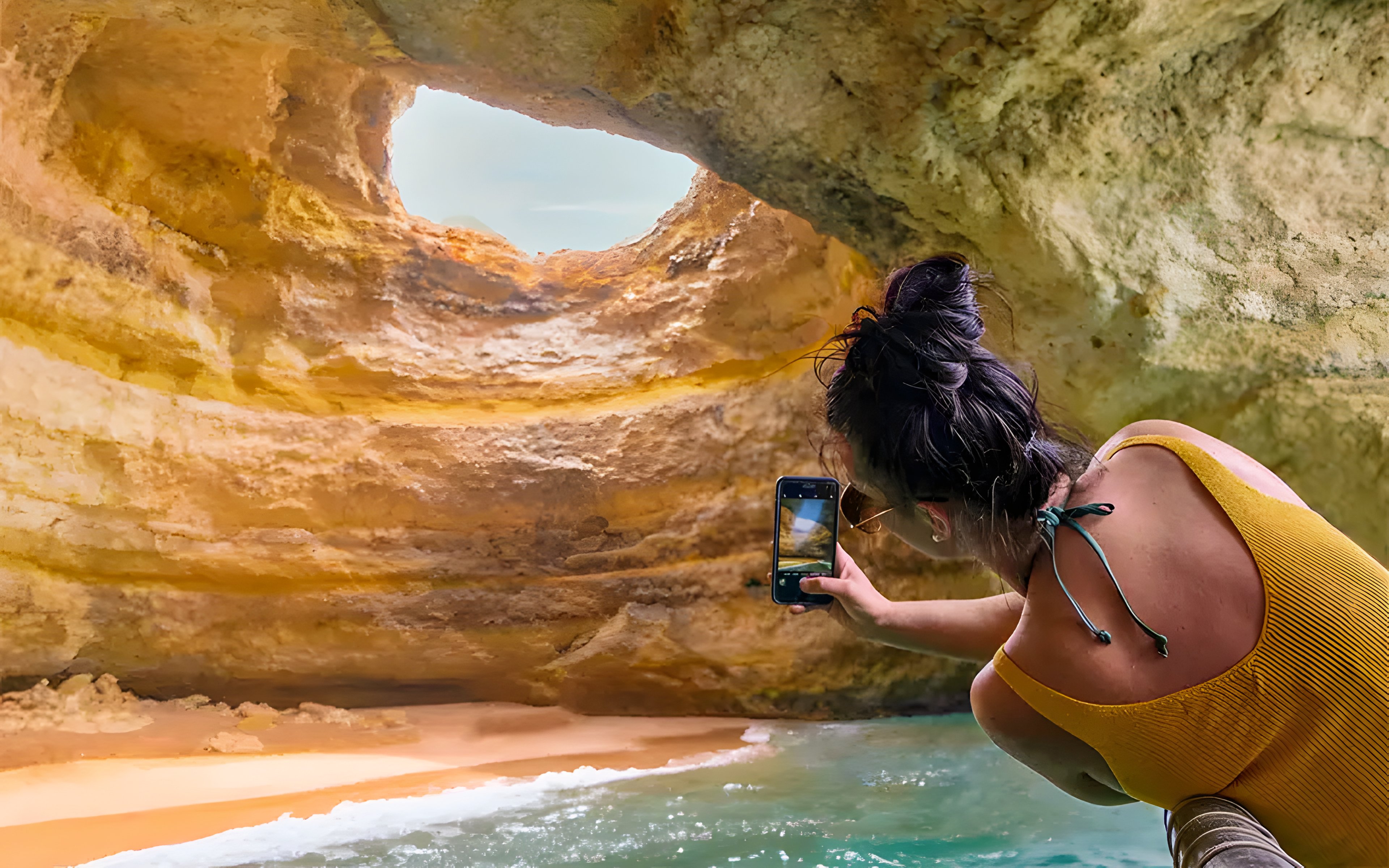 Boat entering Benagil Caves, Algarve, with person taking photo of cave interior.