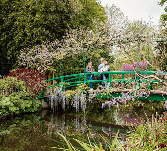 Visitors on a green bridge in Monet's Garden, Giverny, surrounded by blooming flowers.