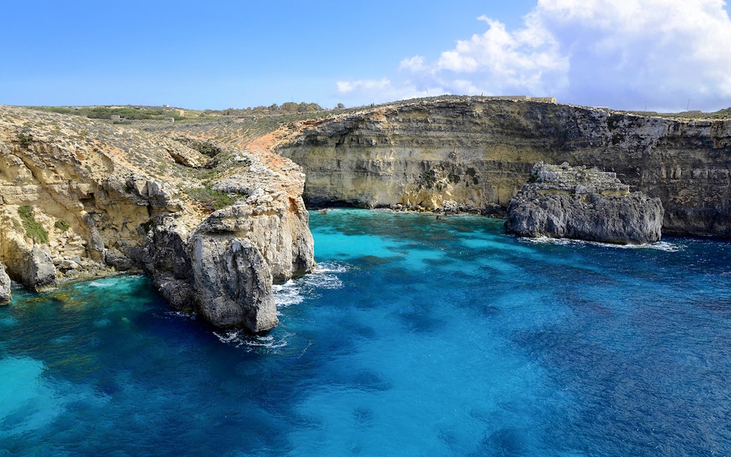 Rocky cliffs and clear blue waters at the Blue Lagoon, Malta.