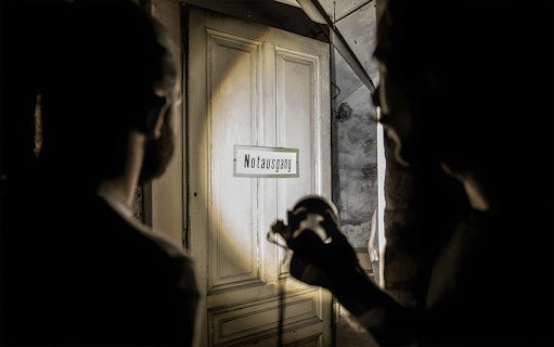 Dimly lit cellar with "Notausgang" sign during Historical Pharmacy Cellar Guided Tour.