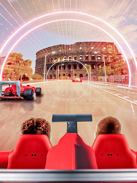 Tourists on a ride at Ferrari Land with a view of a racetrack and Colosseum backdrop.