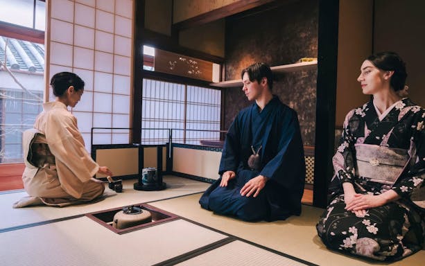 Tourists in kimono participating in a traditional Japanese tea ceremony.