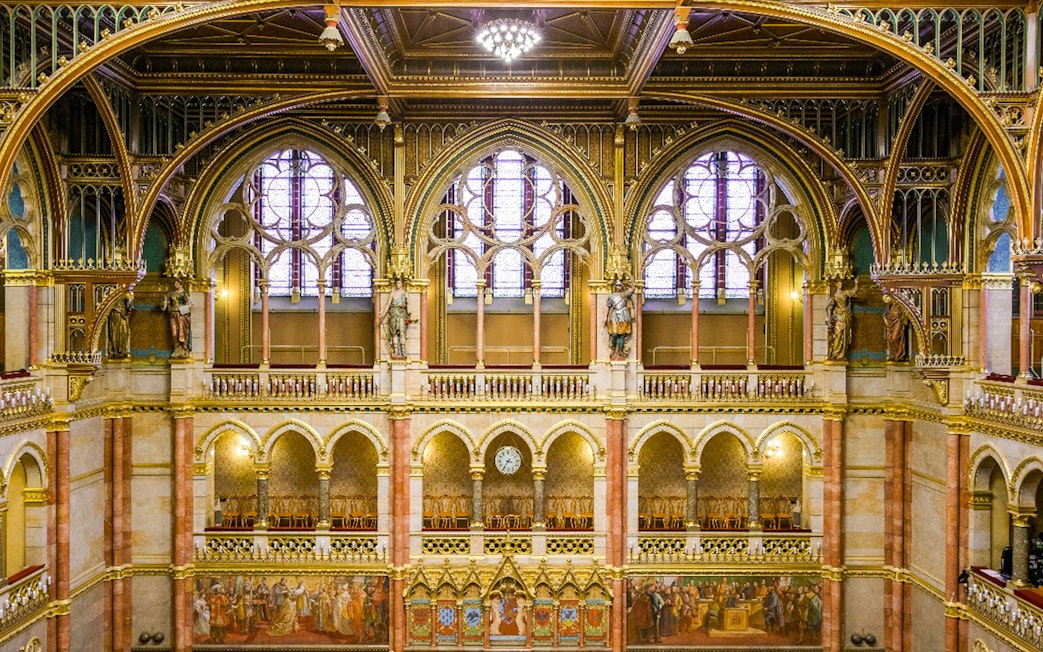 Interior of the House of Peers, Hungarian Parliament, Budapest, showcasing ornate arches and stained glass windows.