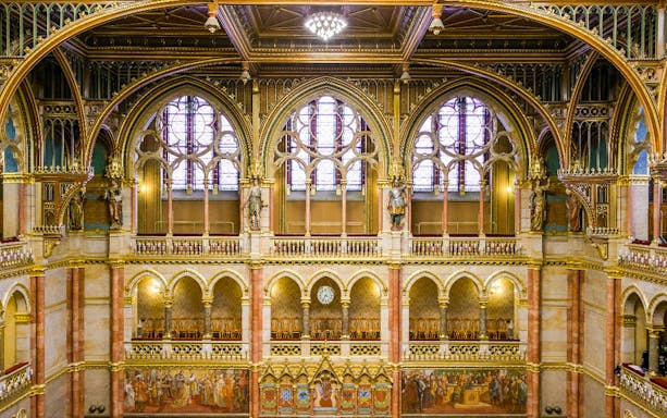 Interior of the House of Peers, Hungarian Parliament, Budapest, showcasing ornate arches and stained glass windows.