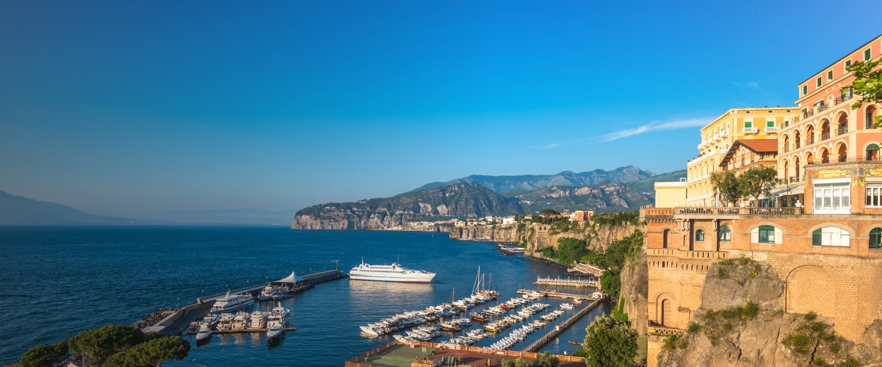 Sorrento coastline with marina, boats, and cliffs under a clear blue sky.