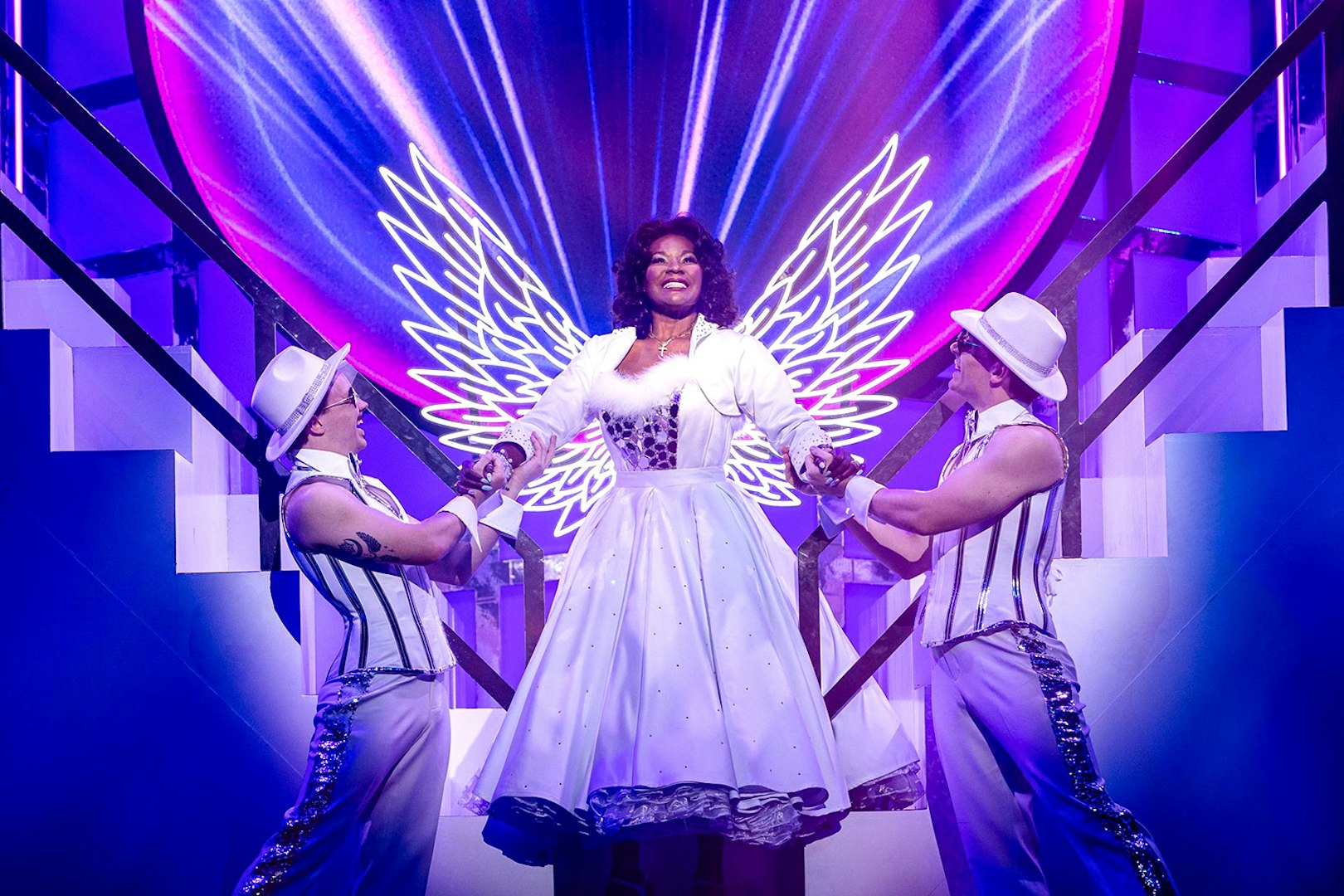 Performer in angel costume with neon wings on stage during Grease musical.