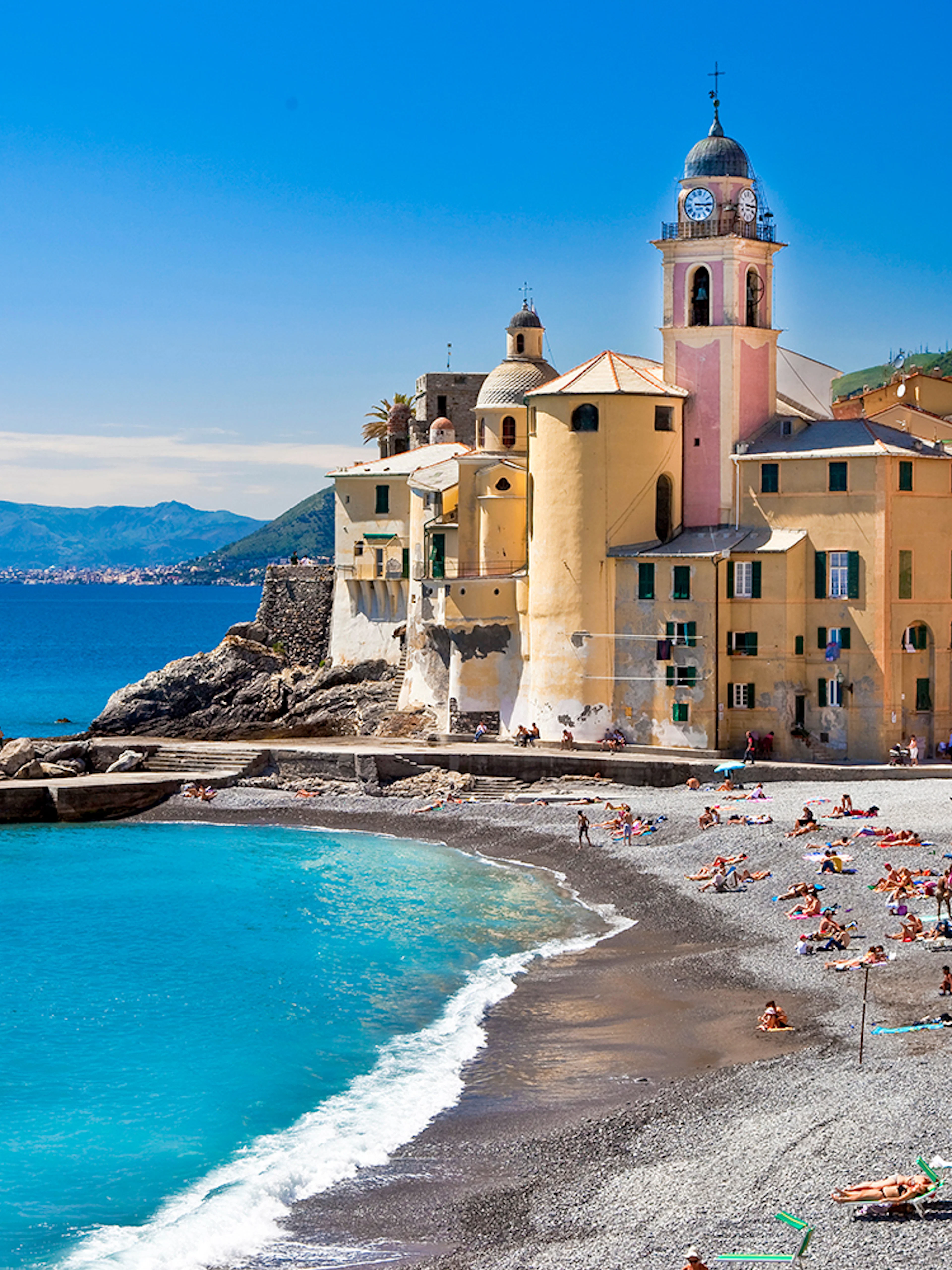 Colorful buildings and beach in Portofino, Italy, with people sunbathing and swimming.