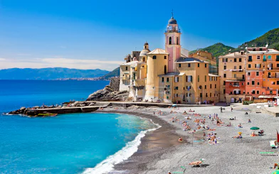 Colorful buildings and beach in Portofino, Italy, with people sunbathing and swimming.