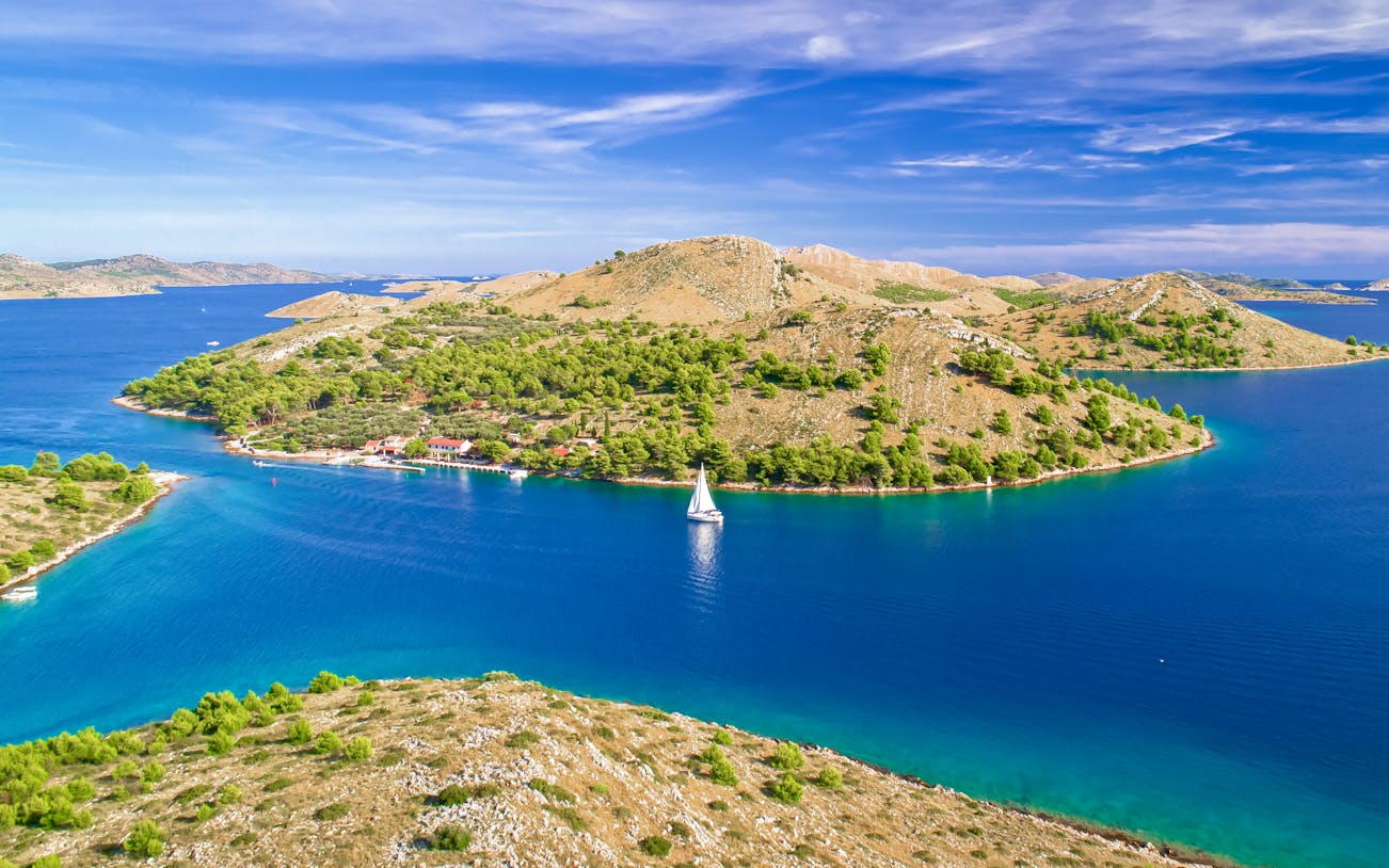 Aerial view of a sailboat near lush islands in Kornati National Park, Adriatic Sea.