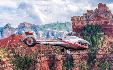 Helicopter flying over Grand Canyon South Rim with red rock formations.