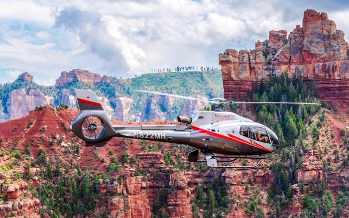 Helicopter flying over Grand Canyon South Rim with red rock formations.