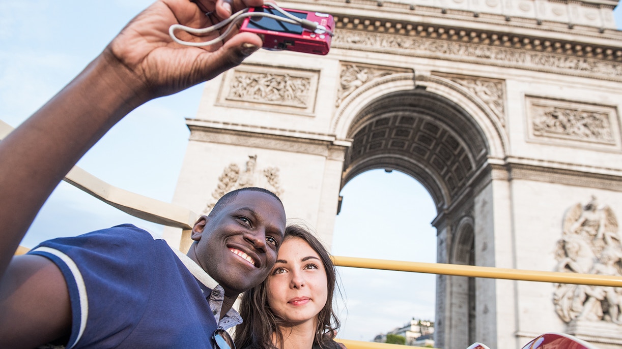 Tourists taking a selfie in front of the Arc de Triomphe during a Paris bus tour.