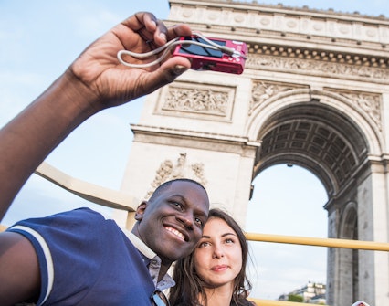 Tourists taking a selfie in front of the Arc de Triomphe during a Paris bus tour.