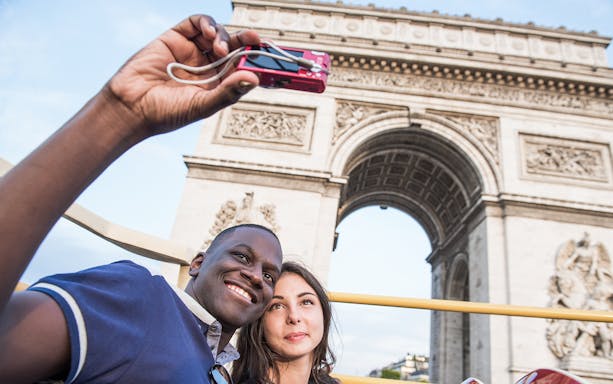 Tourists taking a selfie in front of the Arc de Triomphe during a Paris bus tour.
