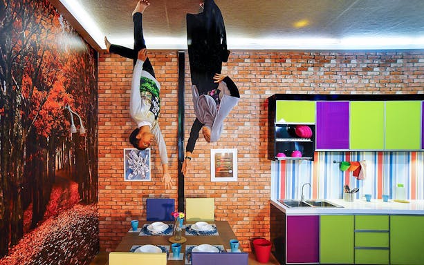 Visitors hanging upside down in a colorful kitchen at the Upside Down House.