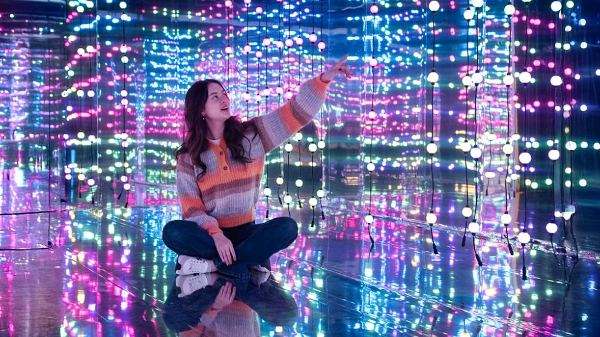 Person sitting in a mirrored room with colorful lights at Dopamine Land, Washington D.C.